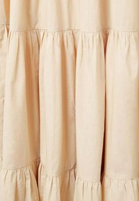 Vaalea beige kangasverho, jossa on rypytettyjä poimuja ja frilla, esittelee sileän tekstuurin ja pehmeän laskeuman.