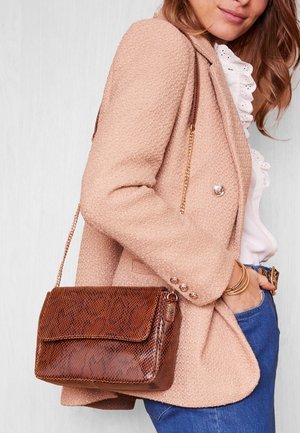 Bruine handtas met slangenpatroon, flap sluiting en gouden kettingriem, gecombineerd met een gestructureerde roze blazer en een witte blouse.