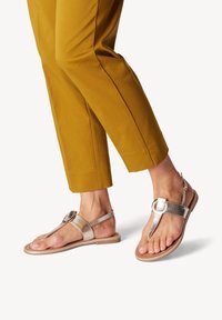 Metalliska silverfärgade sandaler med en tå-postdesign, spänne och en platt sula. Matchade med senapsgula capribyxor.