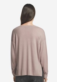 Ljust rosa oversized tröja med en bred halsringning och ribbade ärmslut. Baksidan har en slät yta och går ner under höfterna.