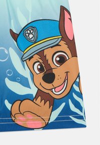 Maillots de bain colorés mettant en avant un chien cartoon portant un chapeau de police bleu, avec un pelage brun et des accents roses, sur fond aquatique bleu.