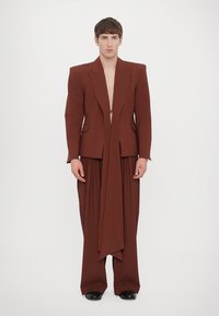 Costum maro, croiat, cu un sacou structurat și pantaloni largi, fluidi. Textură netedă, deschidere frontală și detalii de design minimaliste.