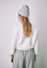 Biely flísový sveter s akcentmi na ramenách, v páse doplnený o sivé nohavice so šnúrkou. Kombinovaný so sivou rebrovanou čiapkou. Jemné textúry a neutrálne farby.