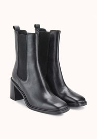 Bottes noires en cuir à hauteur de cheville avec un bout pointu et un talon carré. Dotées de panneaux latéraux élastiques et de languettes pour un enfilage facile. Texture lisse.
