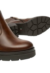 Stivali alla caviglia in pelle marrone con suole in gomma nera, cerniera visibile e marcatura incisa sul fondo "Made in Italy" con una bandiera italiana.