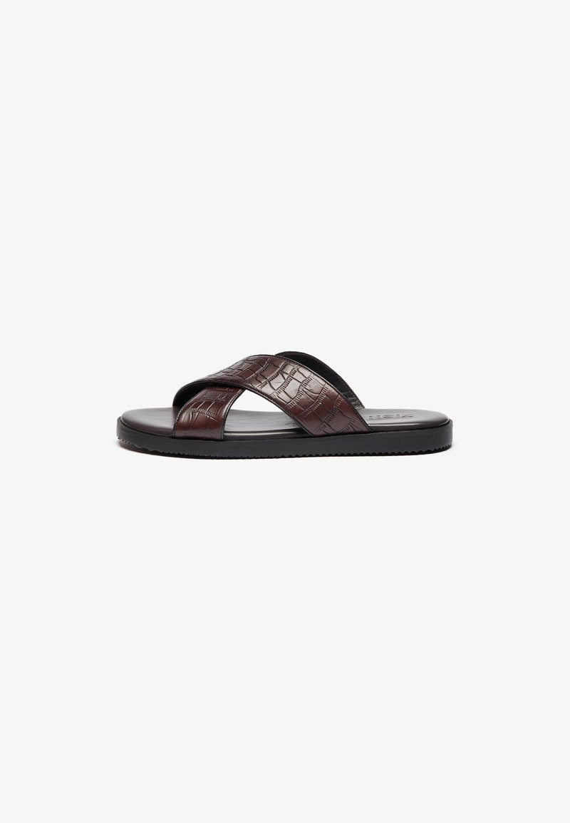 Sandal em napa castanha com tiras cruzadas texturizadas e sola de borracha preta. Apresenta um acabamento suave e um padrão em relevo subtil.