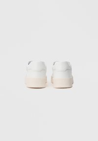 Zapatillas de cuero blanco con una textura suave, forma redonda y suela beige gruesa; diseño minimalista sin patrones ni acentos visibles.