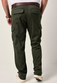 Pantalones cargo de color verde oscuro con un ajuste relajado, que cuentan con bolsillos traseros y laterales, complementados con un cinturón marrón y zapatos blancos.