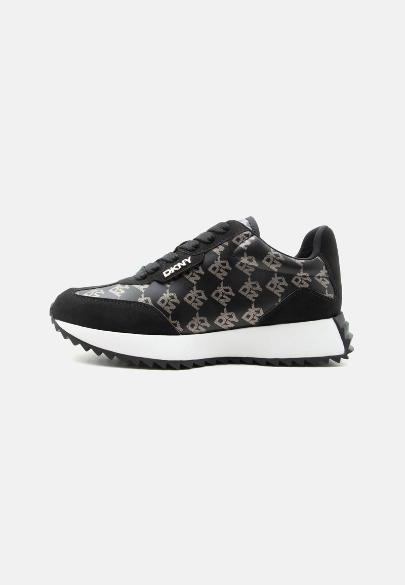 Baskets basses noires avec semelle blanche, décorées de logos "DKNY" répétés et lacets noirs sur fond gris clair.