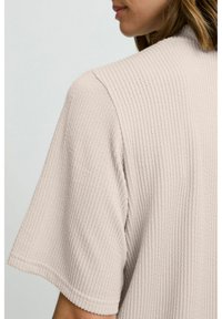 Lys beige tekstureret kortærmet top med et ribbestrik mønster. Stoffet virker blødt og afslappet, med en rund halsudskæring og løs pasform.