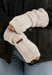 Geknoopte crèmekleurige zondervingerhandschoenen met ribbelstructuur, voorzien van een bruine leren label. Gekocht over een zwarte jas.
