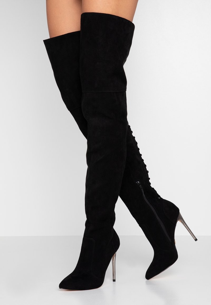 Bottes cuissardes en daim noir avec des talons stilettos hauts, équipées d'une fermeture éclair latérale et d'un détail décoratif à lacets le long de l'arrière.