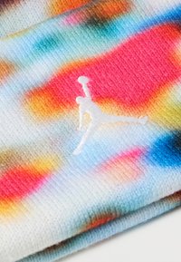 Šarena pletena tkanina koja sadrži kombinaciju pastelno plave, ružičaste, narančaste i žute boje s izvezenim bijelim Jumpman logotipom.