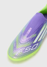 Fotballsko med et lilla og grønt design. Har en teksturert overdel, slip-on stil og fremtredende hvit merkevare. Lett og strømlinjeformet form.