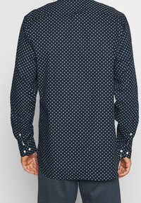 Camicia blu navy a maniche lunghe con motivo geometrico a pois azzurri, polsini con bottoni e orlo arrotondato.