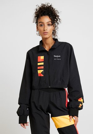 Giacca nera corta con motivi geometrici rossi e gialli, dotata di zip frontale e polsini elastici. Logo Reebok in evidenza.