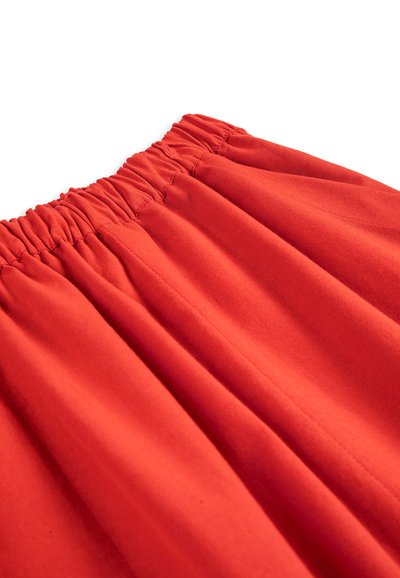 Jupe en tissu rouge vif avec taille élastique froncée et détails de couture verticale apparente.