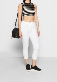 Top corto a righe bianche e nere abbinato a jeans skinny bianchi e sneakers nere. Gli accessori includono una piccola borsa a secchiello nera.