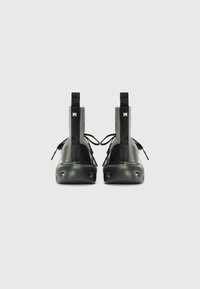 Black high-top shoes with a glossy finish, textured sides, and webbing loops. Features a rounded toe and curved sole with cutouts.
