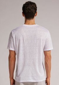 Weißes T-Shirt mit kurzen Ärmeln aus einem leichten, strukturierten Stoff. Verfügt über einen Rundhalsausschnitt und eine lockere Passform, mit sichtbaren Nähten an den Säumen.