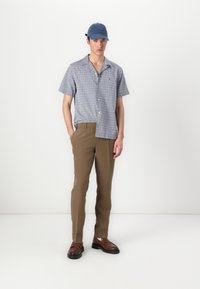 Camicia a maniche corte, azzurra a fantasia, pantaloni color sabbia e mocassini marroni. Include un berretto blu con dettagli logati, vestibilità su misura e tessuto morbido.