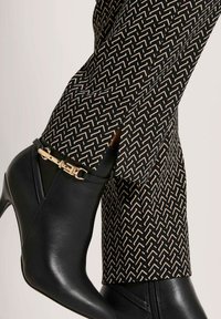 Zwarte leren enkellaarzen met gouden gespdetails, gecombineerd met zwart en beige gestreepte broek.