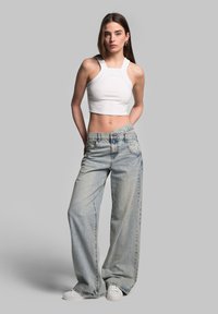 White ribbed crop top with wide straps paired with light blue wide-leg jeans and white sneakers, showcasing a relaxed fit and casual style.