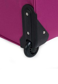 Esquina de una maleta de tela púrpura con una base de plástico duro negro y una rueda giratoria, con tornillos de metal plateado y una superficie texturizada.