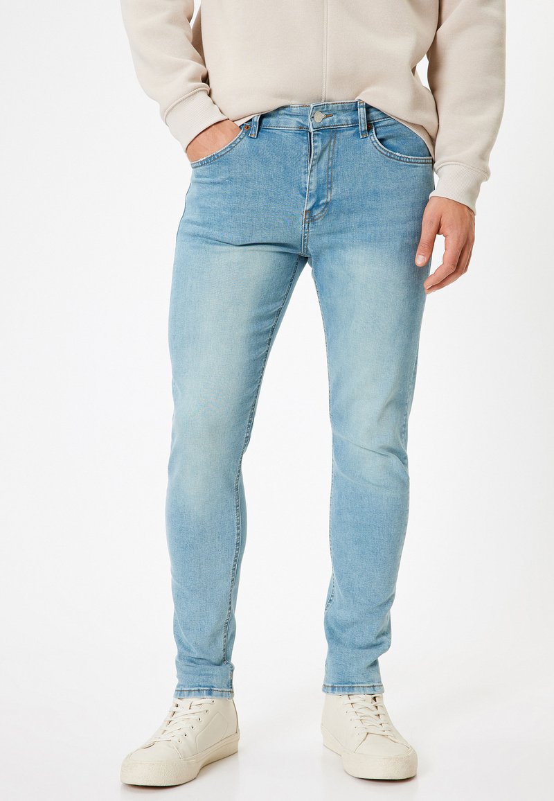 Ljusblå denimjeans med slim fit, femficksdesign och subtil blekning. Matchas med krämfärgade sneakers för kontrast.