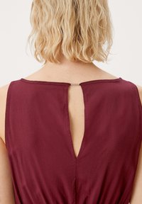 Vestido sin mangas burdeos con detalle de abertura en la espalda, que presenta una textura suave y un escote redondo. La tela parece ligera y fluida.