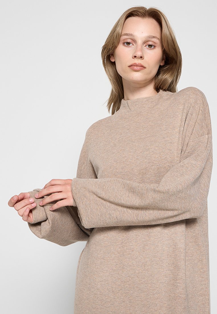 Beiger, übergroßer Pullover mit langen Ärmeln und gerippter Textur. Hoher Kragen mit zartem Nahtdetail. Weicher Stoff und entspannter Schnitt.