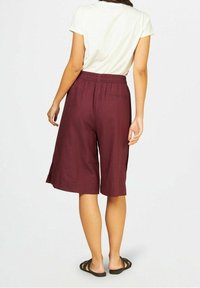 Burgundské kalhoty culottes vyrobené z lehkého materiálu, s elastickým pasem a bočními rozparky pro zvýšenou pohyblivost, doplněné černými sandály.