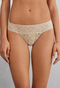 Lace bikini slipjes in een natuurlijke tint, met bloemmotieven, een brede kanten tailleband en een soepele, zachte textuur.