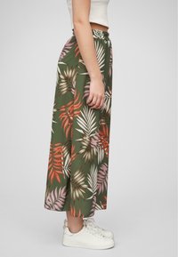 Maxi gonna verde con motivo a foglie tropicali in rosso, rosa e bianco; vita elastica; abbinata a sneakers bianche.