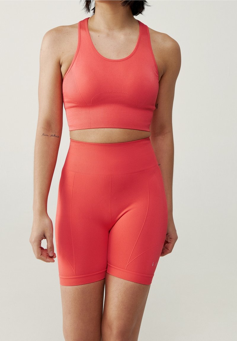 Korálový bezšvový sportovní crop top a vysoké šortky, které se vyznačují ribbovanou texturou a přiléhavým střihem.