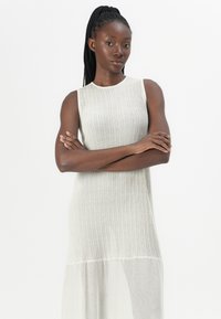Sleeveless dress in light gray, featuring a ribbed texture on the upper part and a sheer, flowing lower section. Simple, straight silhouette.
