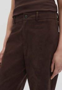 Braune Wildlederhosen mit flachem Frontdesign, seitlichen Taschen und einem Knopfverschluss, bieten eine glatte Textur und eine lockere Passform.