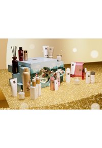 Sammlung von Hautpflegeprodukten auf einer goldenen, funkelnden Oberfläche. Umfasst Flaschen, Gläser und eine Kerze, die verschiedene Formen, Farben und Texturen aufweisen.