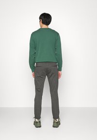 Grøn langærmet skjorte, grå tapered bukser og grønne sneakers. Enkel design, bomuldsstof med glat tekstur. Neutral baggrund.