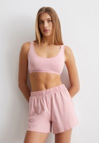 Roze katoenen bralette met brede bandjes, gecombineerd met bijpassende shorts met elastische taille. Beide hebben een soepele textuur en een ontspannen pasvorm.