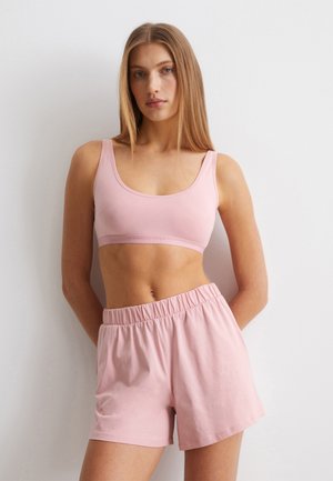 Roze katoenen bralette met brede bandjes, gecombineerd met bijpassende shorts met elastische taille. Beide hebben een soepele textuur en een ontspannen pasvorm.