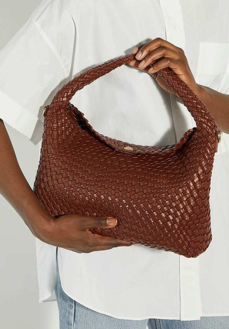 Brown woven handbag with a curved handle, textured surface, and subtle sheen. Features a magnetic closure and sits against a white shirt.