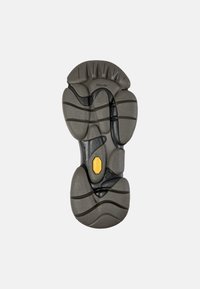 Suola Vibram grigia con motivi testurizzati, accentuata da un logo giallo e profonde scanalature per la trazione. Design curvo con molteplici contorni.