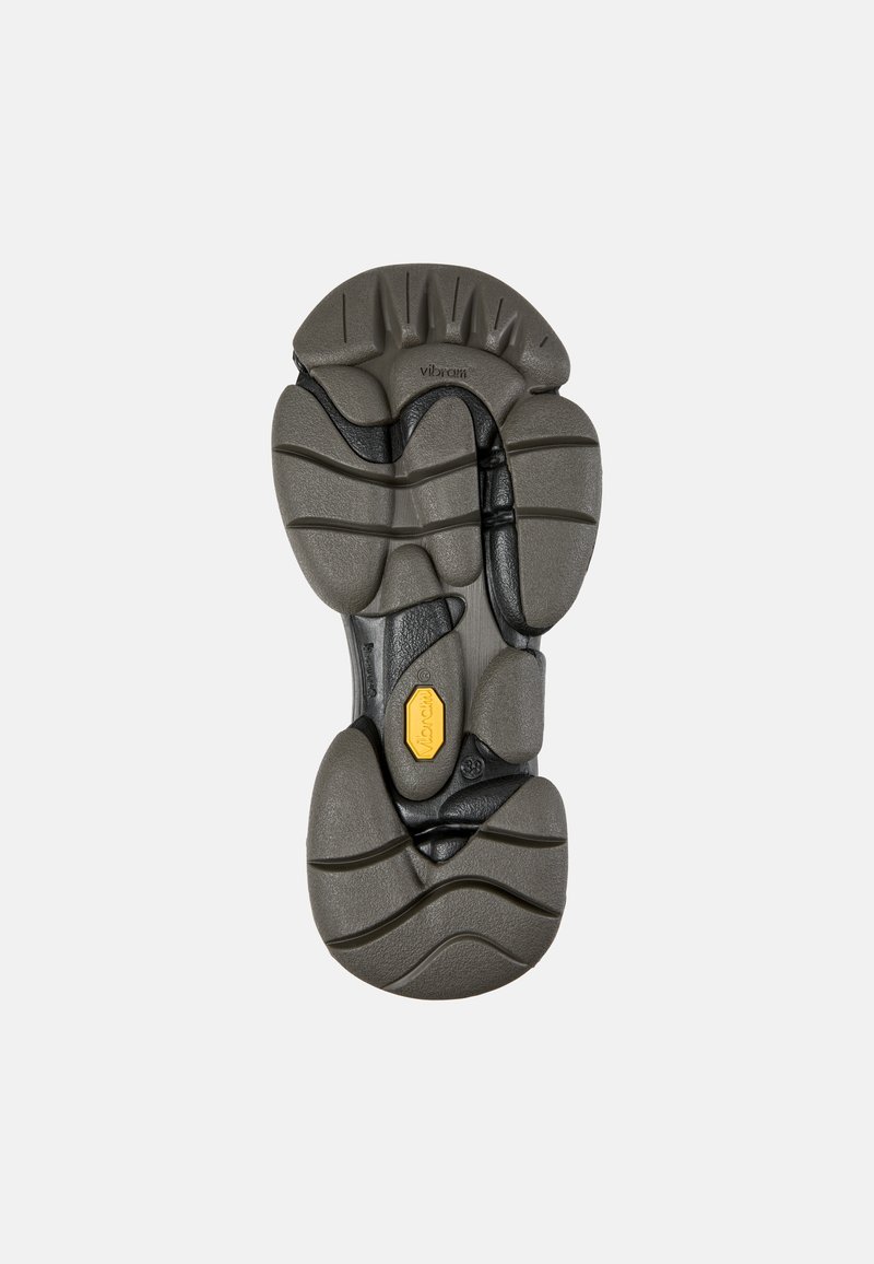Graue Vibram-Sohle mit strukturierten Mustern, einem gelben Logoakzent und tiefen Rillen für Traktion. Detailliertes Design mit mehreren Konturen.