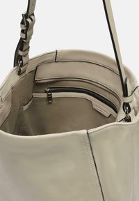 Jasnoszara skórzana torebka z otwartym wnętrzem. Posiada kieszeń na zamek, gładką fakturę oraz kompozytowy pasek o regulowanej długości.