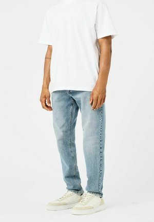 Witte T-shirt met korte mouwen, gecombineerd met lichtblauwe denim jeans en crèmekleurige sneakers met beige accenten. Eenvoudige, casual outfit.