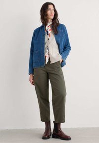 Veste en denim, pull en tricot beige, écharpe colorée, pantalon vert olive et bottines brunes. Design simple avec poches et textures contrastantes.