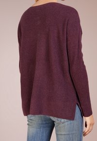 Vinröd, ribbad stickad tröja med vid halsringning, långa ärmar och sidslitsar; satt ihop med ljusblå denimjeans.