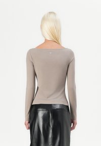 Bluză cu mânecă lungă dintr-un material moale, de culoare taupe, cu un decolteu larg și jos, având un detaliu cu logo la spate. Asortată cu o fustă din piele neagră.