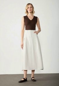 Brown sleeveless top paired with a white pleated midi skirt, featuring side pockets and a flowy design, complemented by black flat shoes.